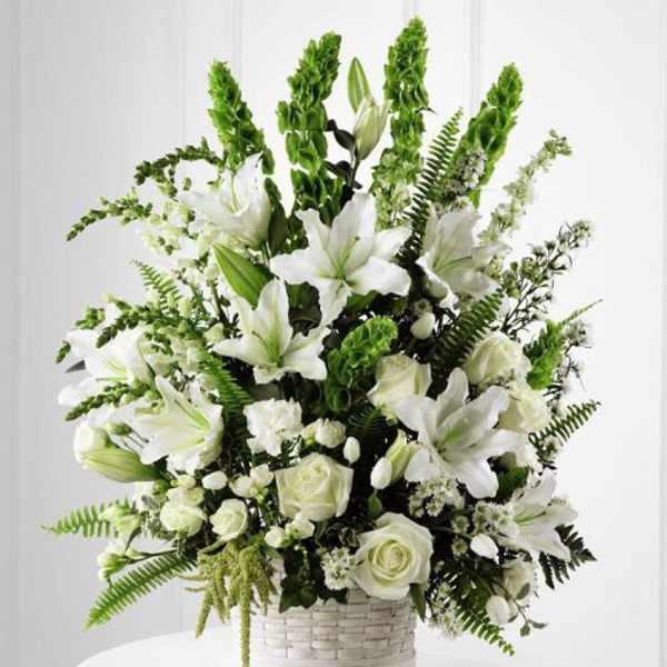 White lilies and roses arranged in a white basket with green accents
