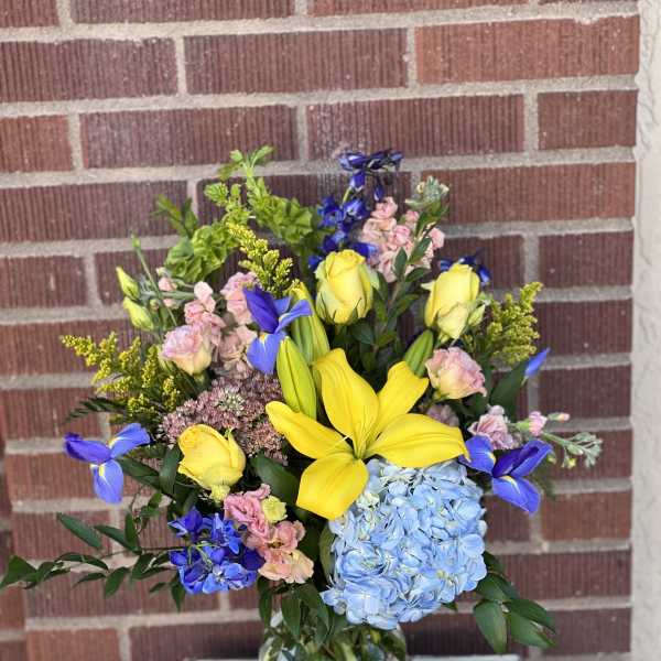 Mixed bouquet with yellow lilies, blue hydrangea, and pink flowers in a glass vase