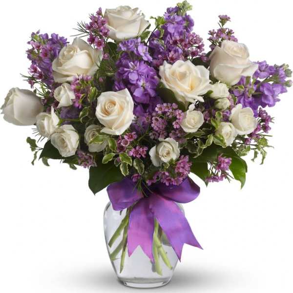 White roses and purple flowers in a glass vase with a purple ribbon