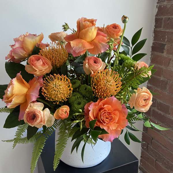 Orange and peach floral arrangement in a white vase