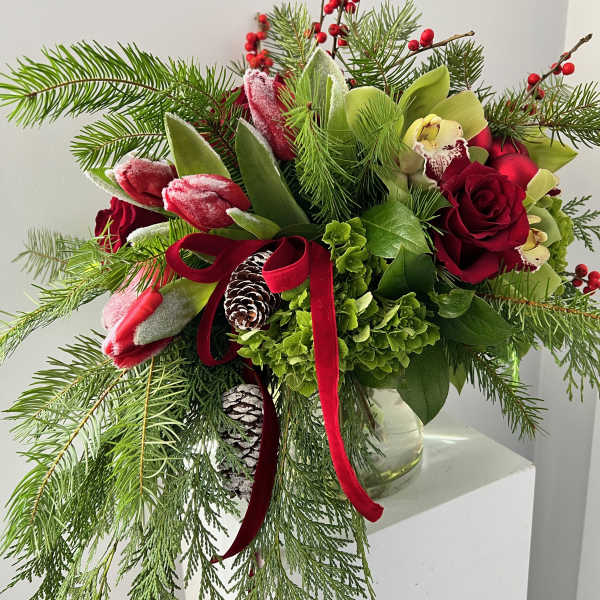 Holiday bouquet with red roses, tulips, and evergreen branches in a glass vase