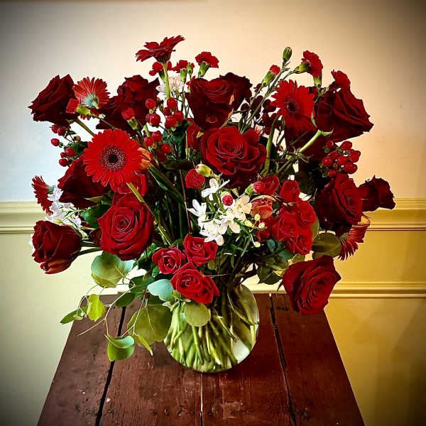Large arrangement of red roses and gerbera daisies in a round glass vase
