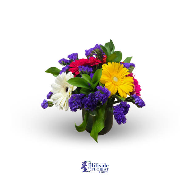 Short bouquet of yellow, red, pink, and white gerbera daisies with purple filler in a glass vase