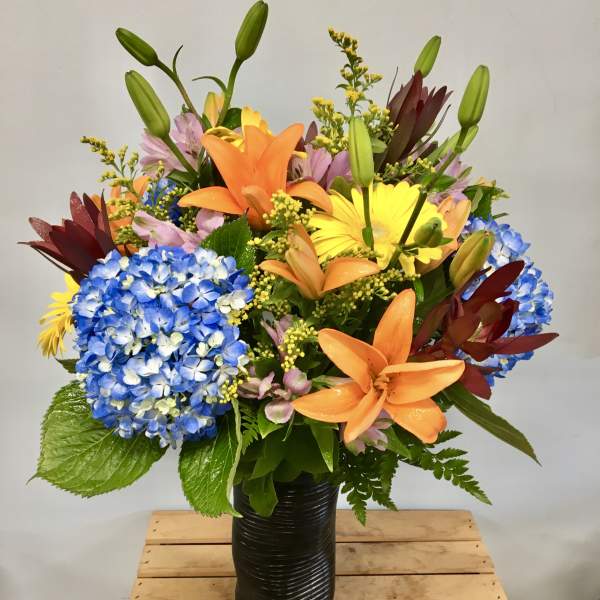 Colorful bouquet with lilies, hydrangeas, and gerbera daisies in a black vase