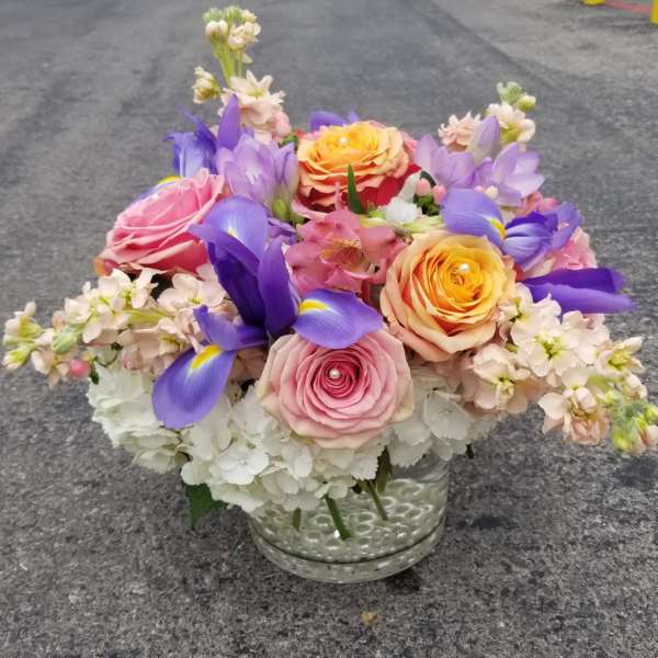 Mixed bouquet of roses, irises, and white blooms in a glass vase