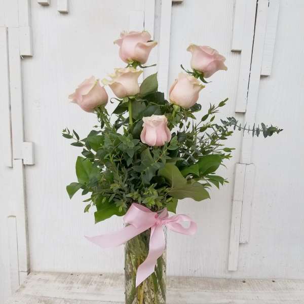 Tall bouquet of pale pink roses in a glass vase with a pink ribbon