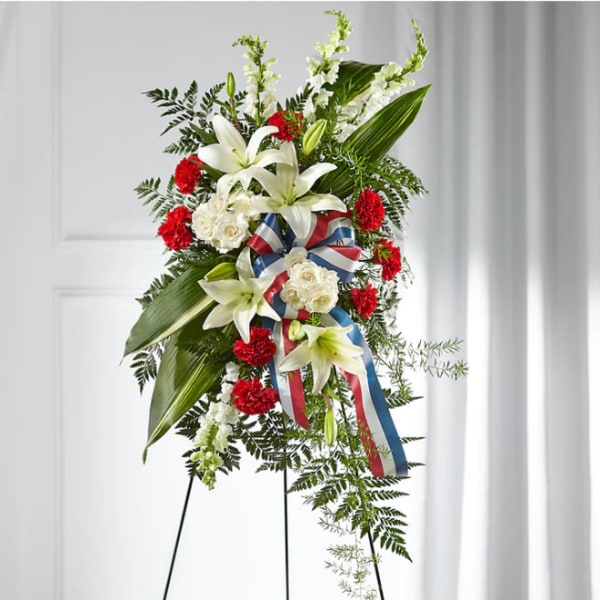 Standing floral spray with white lilies, red carnations, and ribbon on an easel