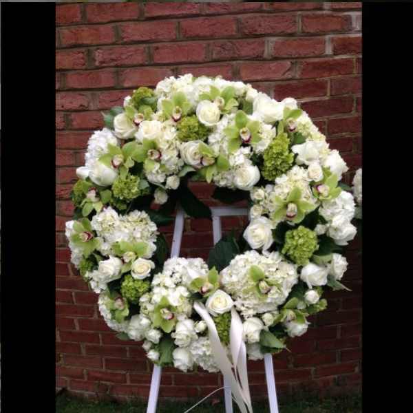 Large white floral wreath with green accents on a stand