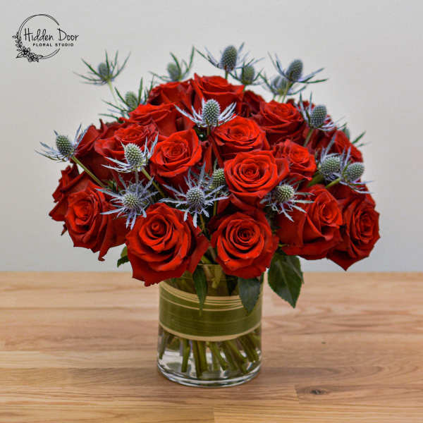 Red roses arranged in a glass vase with blue thistle accents