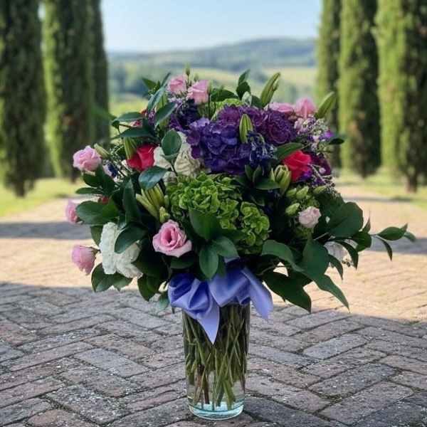 Bouquet of pink and purple flowers in a clear glass vase with a lavender ribbon