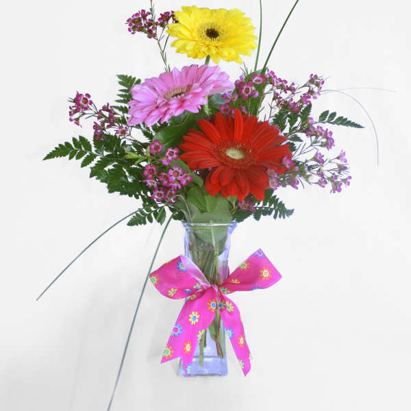 Gerbera daisy bouquet in a glass vase with a pink ribbon