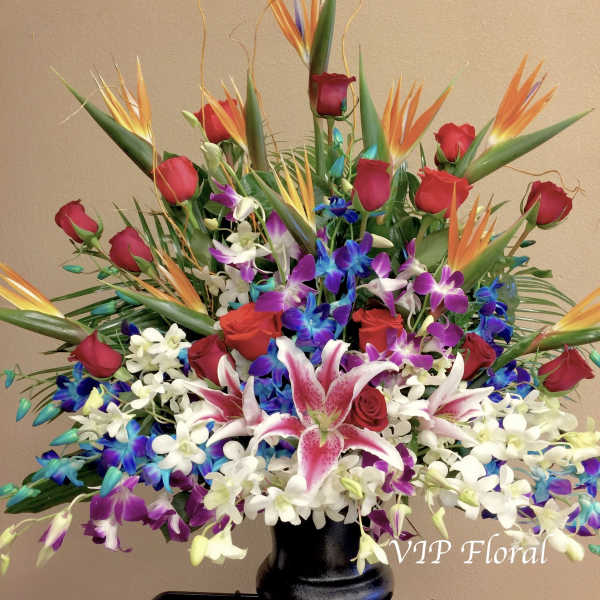 Large tropical bouquet with red roses, orchids, and bird of paradise in a black vase