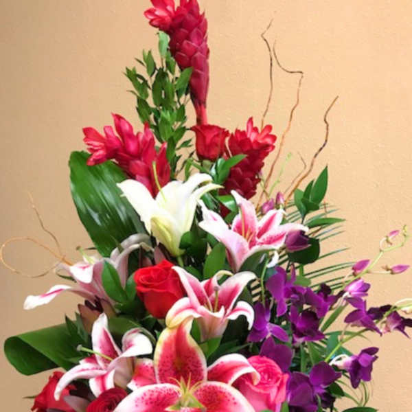 Tall floral arrangement with pink lilies, red roses, and purple orchids in a white container