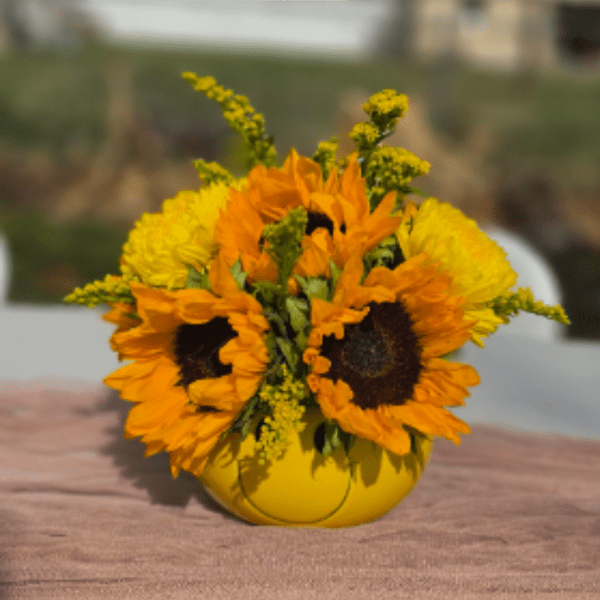 Compact arrangement of bright sunflowers and yellow blooms in a round yellow vase