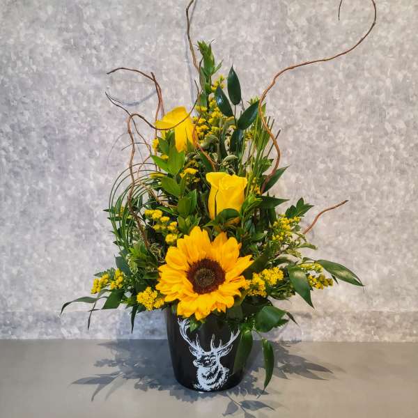 Sunflower and yellow rose arrangement in a black deer-print container