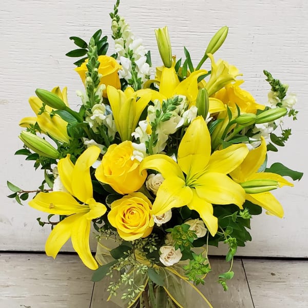 Yellow lilies and roses arranged in a clear glass vase