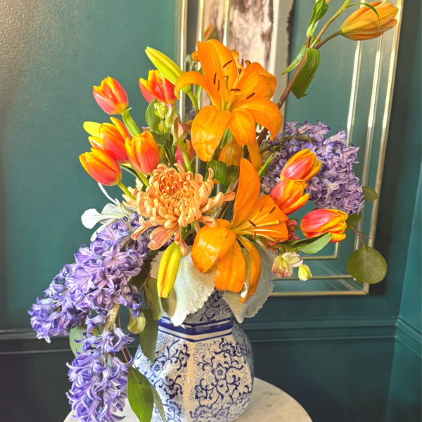 Bright orange lilies, tulips, chrysanthemum, and purple hyacinths in a blue and white ceramic vase