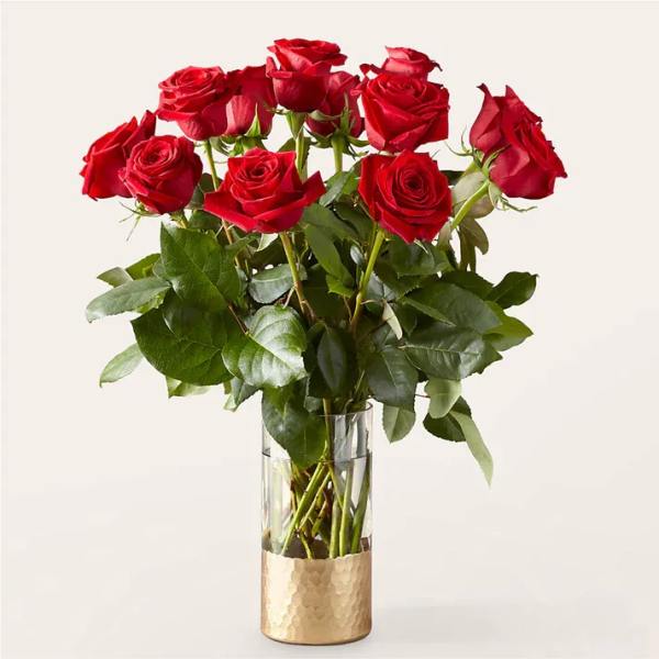 Red roses arranged in a clear glass vase with a gold base