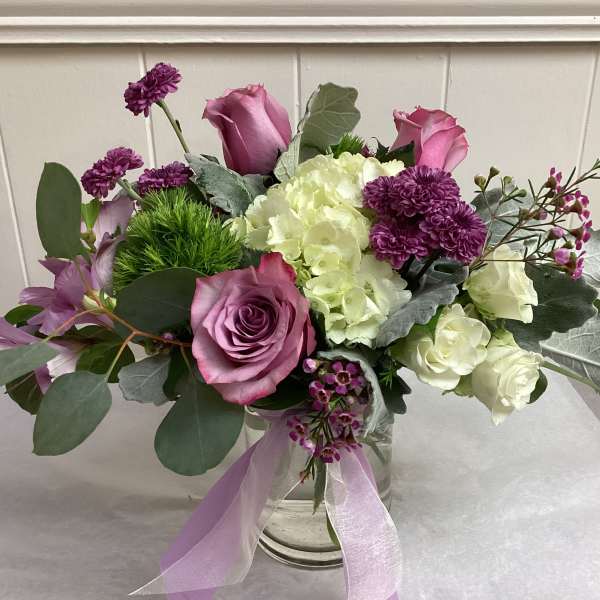 Pink and white floral arrangement in a clear glass vase with a lavender ribbon