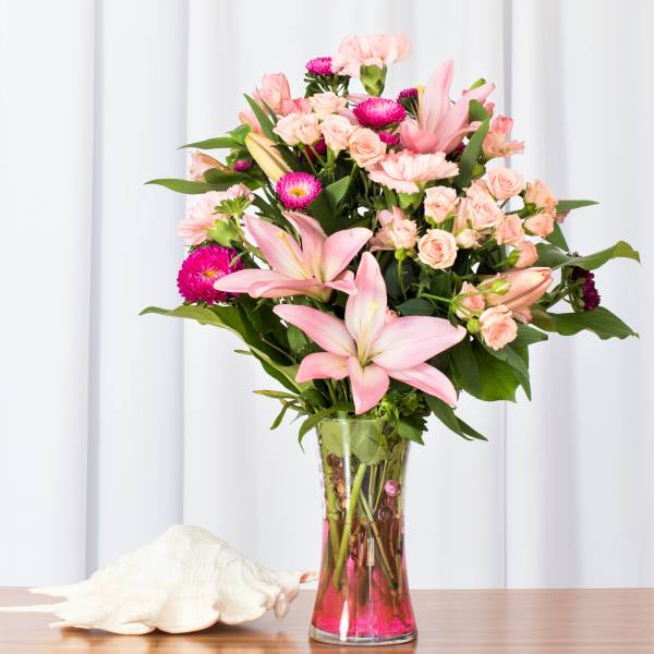 Tall bouquet of pink lilies, carnations, and spray roses in a clear vase with pink water