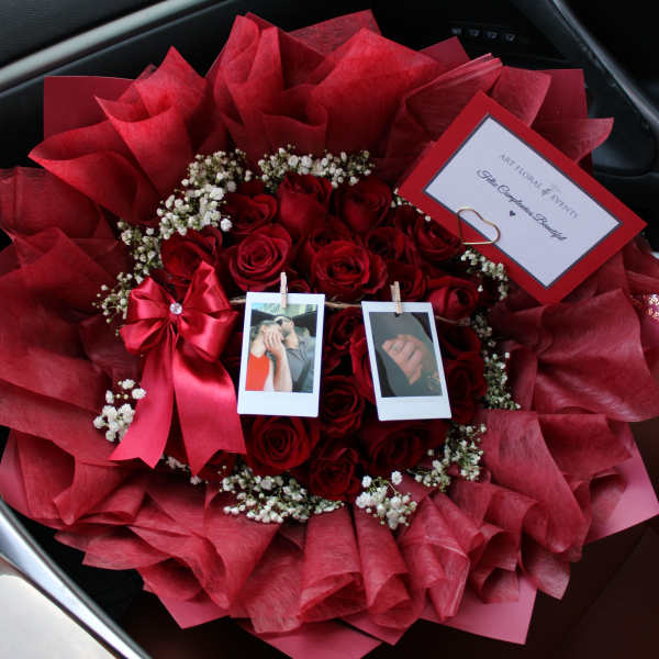 Bouquet of red roses with baby’s breath, ribbon, and photo clips in a car seat