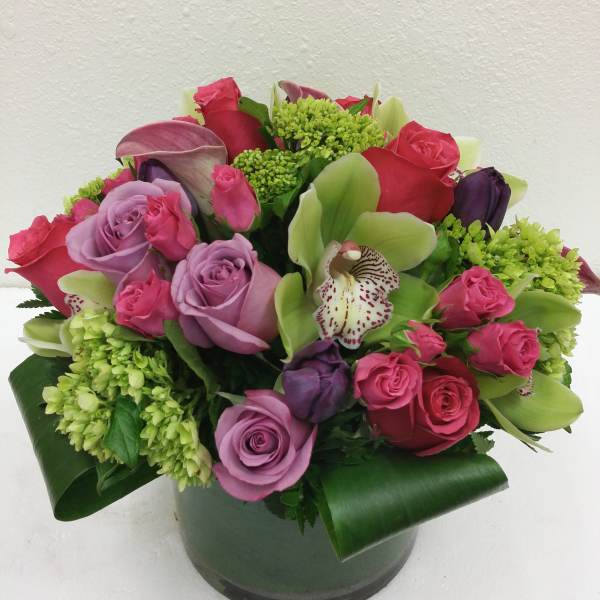 Pink and lavender roses with green orchids in a round vase