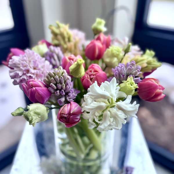Mixed bouquet of pink tulips and pastel hyacinths in a clear glass vase.