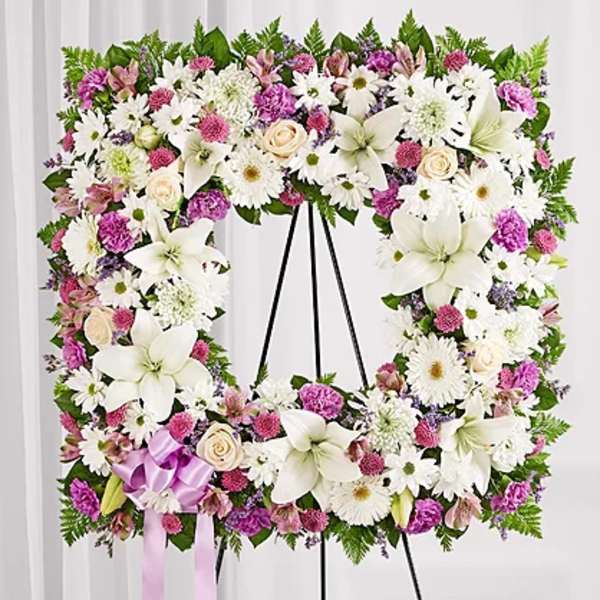 Floral standing wreath with white lilies, daisies, and pink blooms on an easel