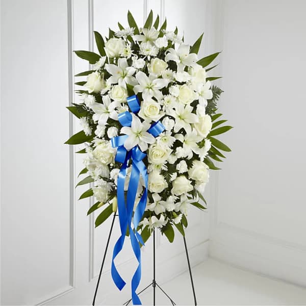 White funeral spray with roses and lilies on a stand, accented by a blue ribbon
