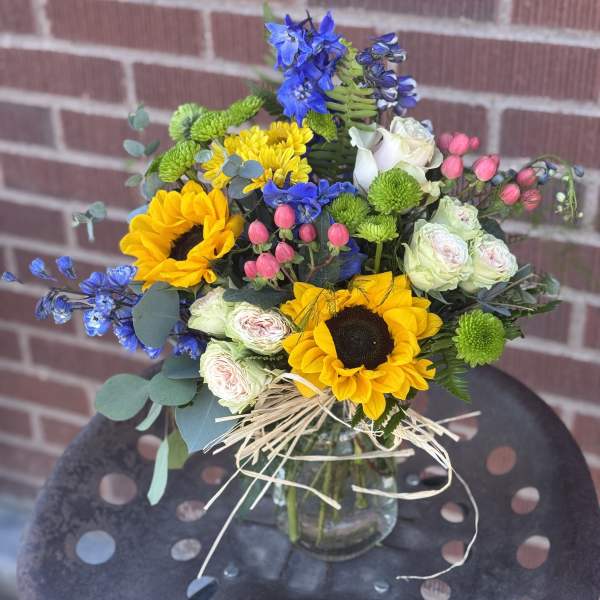Mixed bouquet with sunflowers, blue flowers, and pale roses in a glass vase