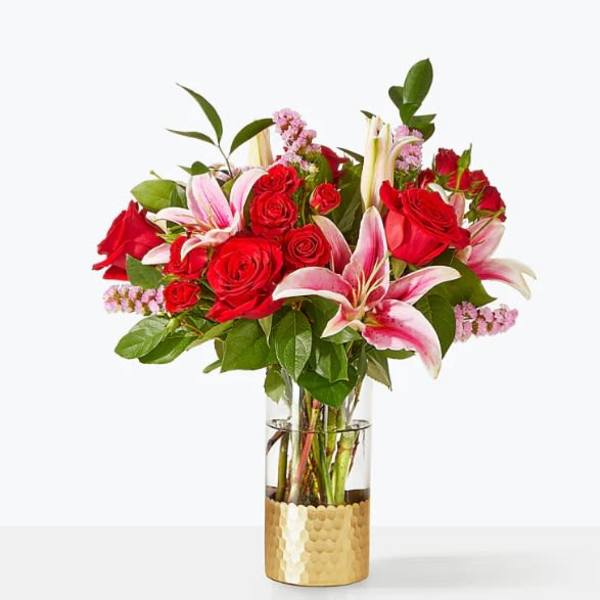 Red roses and pink lilies arranged in a glass vase with a gold base.