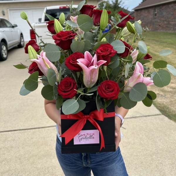 Bouquet of red roses and pink lilies in a black gift box with a red ribbon