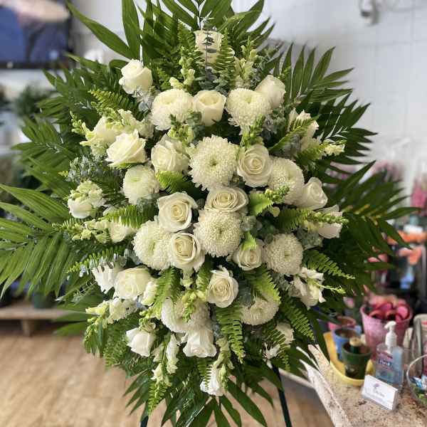 Large white floral spray with roses and round mums surrounded by palm fronds