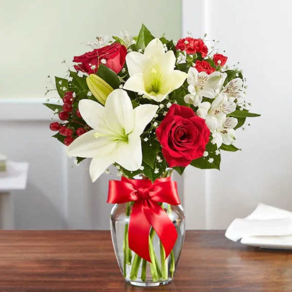 Bouquet of red roses and white lilies in a glass vase with a red ribbon
