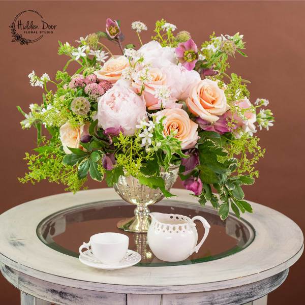Pink and peach rose arrangement in a glass vase with a teacup and creamer