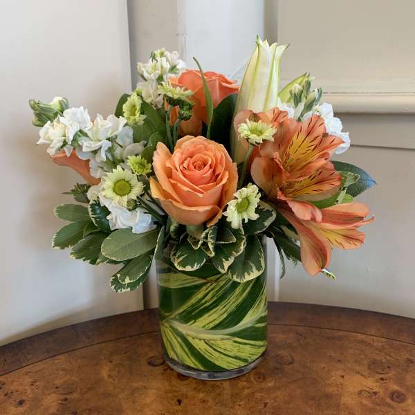 Orange roses and white flowers in a green glass vase