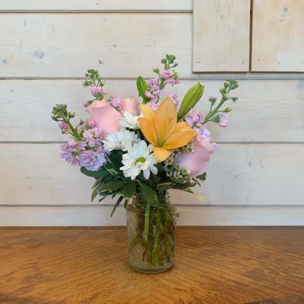 Pink and yellow flowers arranged in a glass jar vase