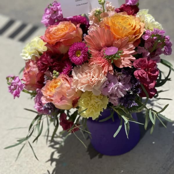 Mixed bouquet of roses, gerbera daisies, and carnations in a purple vase