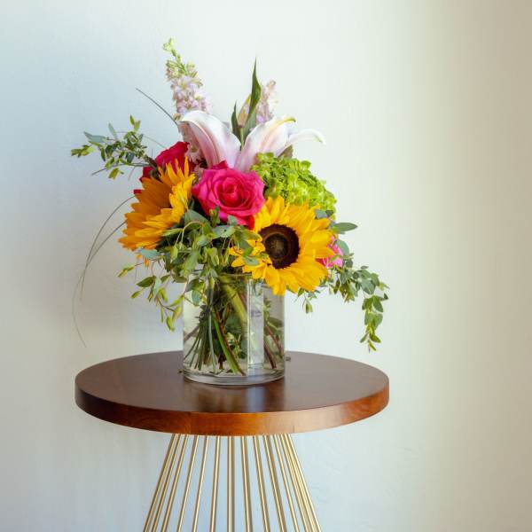 Mixed bouquet in a clear glass vase with sunflowers, roses, and lilies