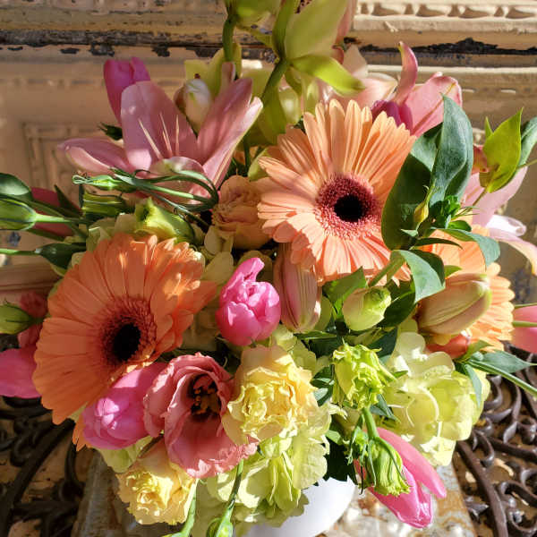 Bouquet of peach gerbera daisies, pink lilies, and pale green blooms in a white vase