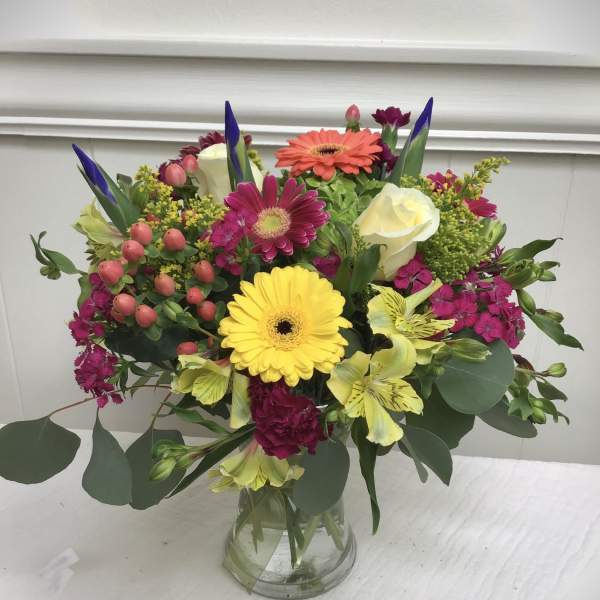 Bright mixed bouquet of gerbera daisies, roses, and other blooms in a clear glass vase