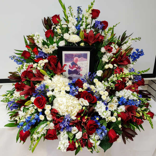 Large funeral wreath of red, white, and blue flowers with a framed photo in the center