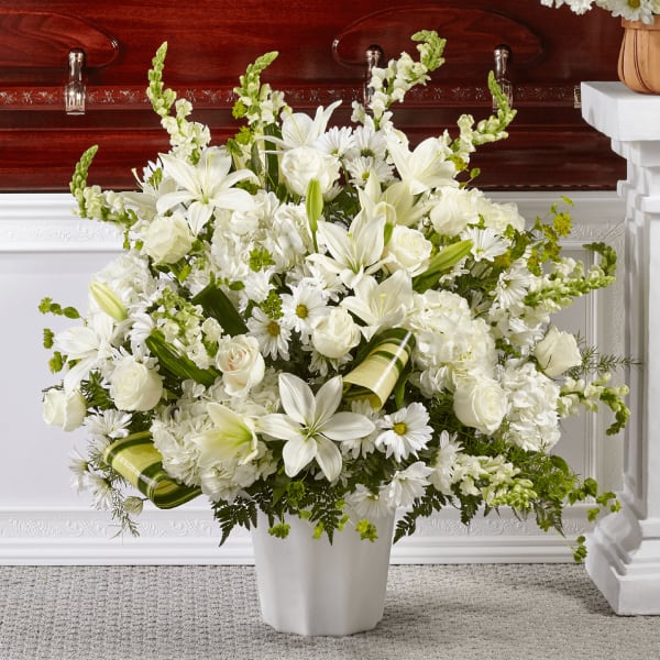 White lilies, roses, and daisies arranged in a white vase