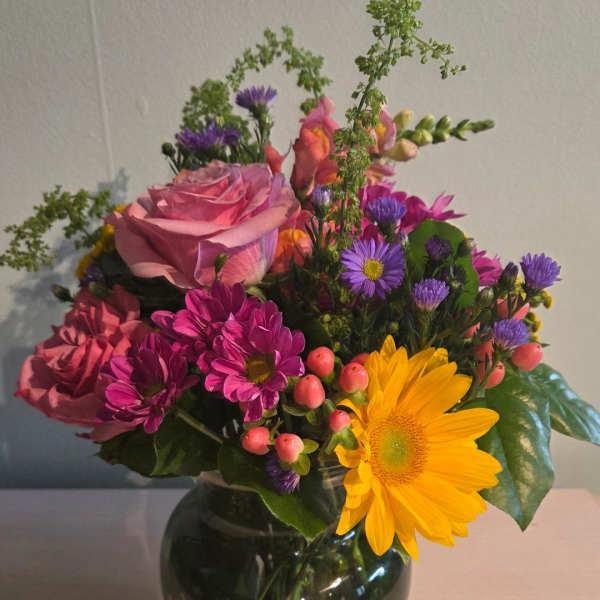 Mixed bouquet of pink roses, purple daisies, and a yellow gerbera in a glass vase