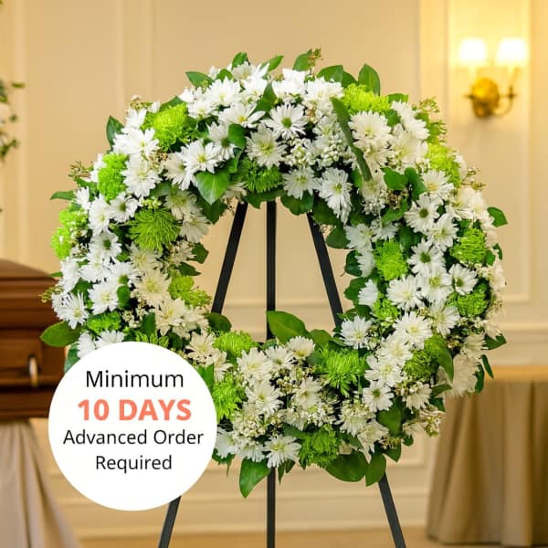 Large white and green floral wreath on a black metal easel in a chapel.