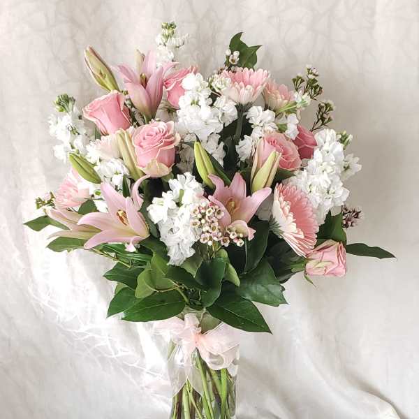 Pink lilies and roses arranged in a clear glass vase with white filler flowers.