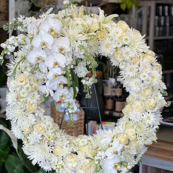 Large white and cream floral wreath with roses, orchids, and mums on a stand