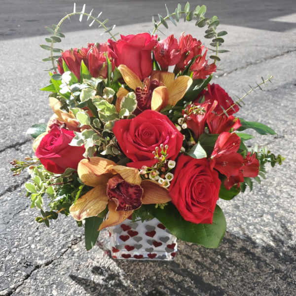 Red roses and orchids arranged in a heart-shaped bouquet in a heart-patterned vase