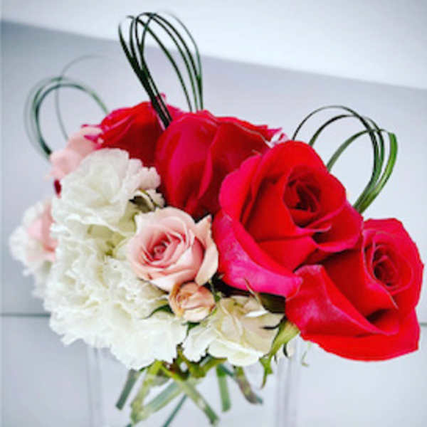 Red and pink roses with white carnations in a clear glass vase