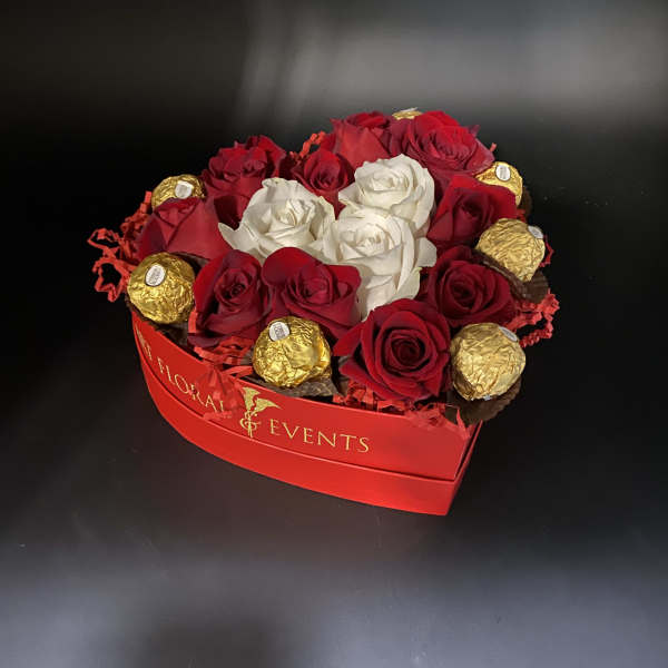 Red and white roses arranged with gold-wrapped chocolates in a red box